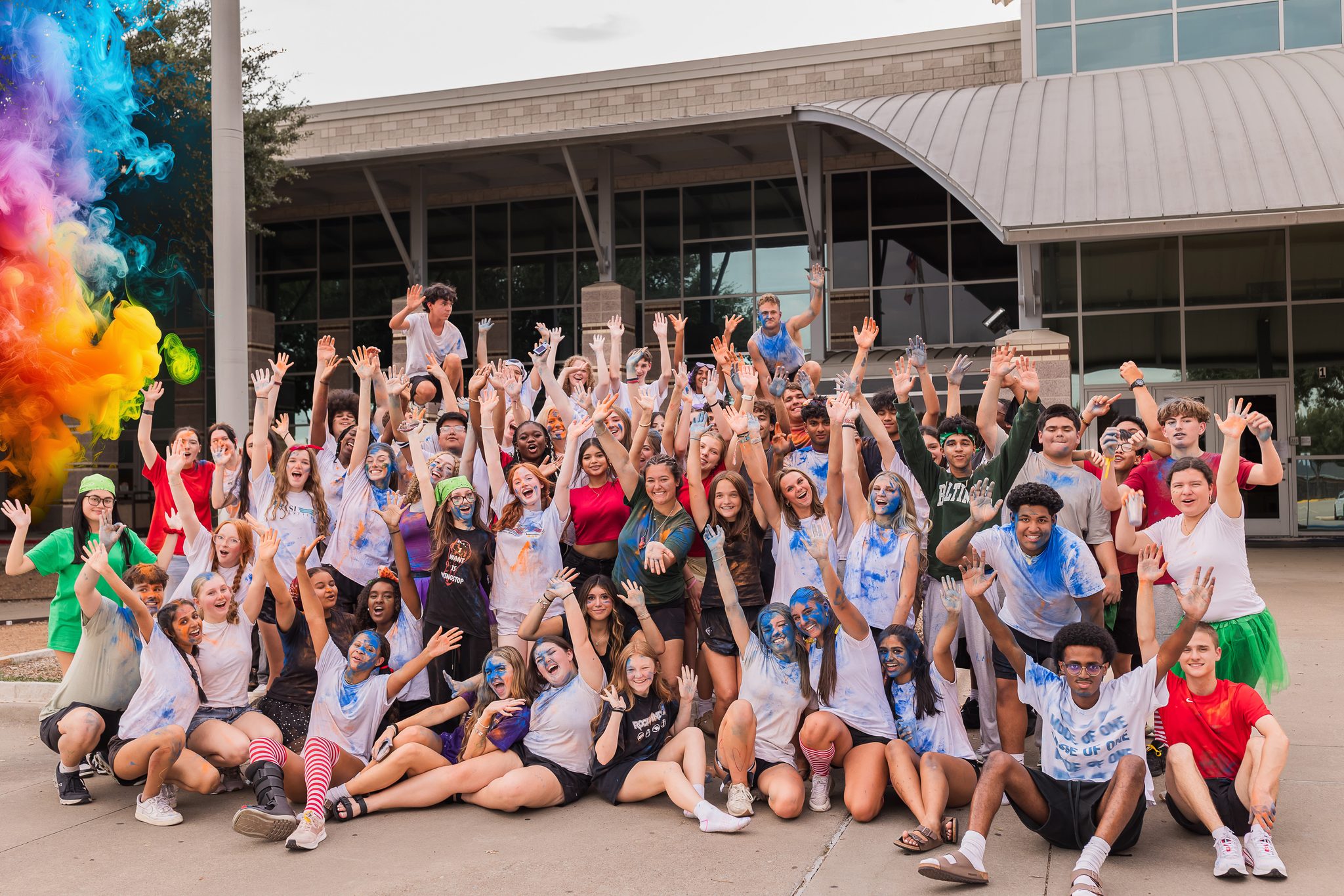 Sachse Choir students covered in colored powder, cheering together outside Sachse High School